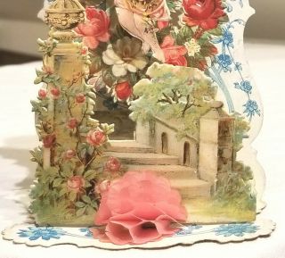 Cupid hovering over Victorian Flower Garden.  3 - dimensional Card.  Early 1900s. 3